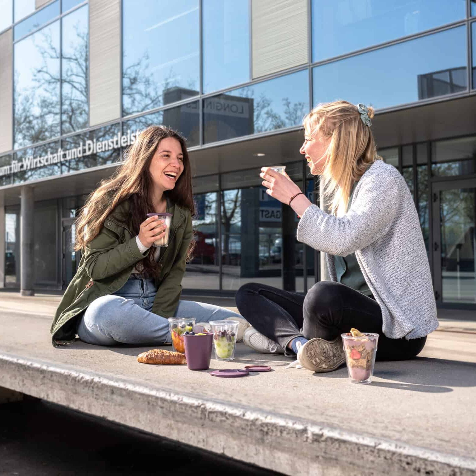 zwei Frauen sitzen lachend am Boden und trinken aus einem ISY Becher